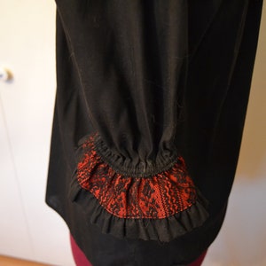 May include: Black blouse with a red and black lace trim on the sleeves.