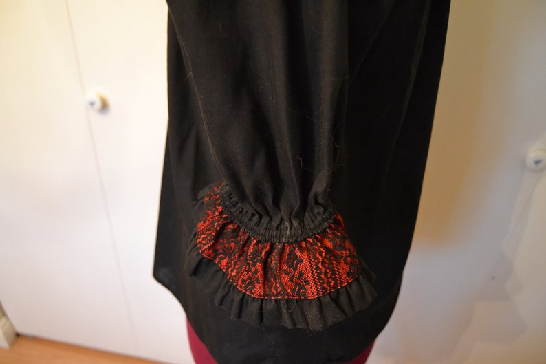 May include: Black blouse with a red and black lace trim on the sleeves.