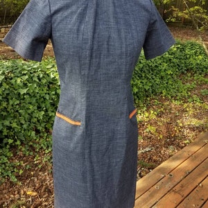 May include: A blue denim dress with orange trim around the collar and pockets. The dress has short sleeves and a fitted silhouette.