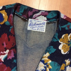 May include: A dark blue denim jacket with a floral print. The jacket has a label that reads "Rockmount Ranch Wear Denver Colo. Made in U.S.A."