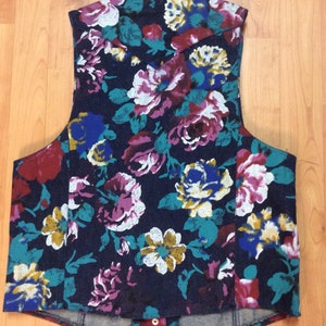 May include: A sleeveless vest with a floral print in shades of blue, red, white, and yellow on a dark blue background. The vest has a pointed collar and a button closure.