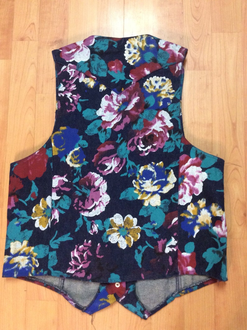 May include: A sleeveless vest with a floral print in shades of blue, red, white, and yellow on a dark blue background. The vest has a pointed collar and a button closure.