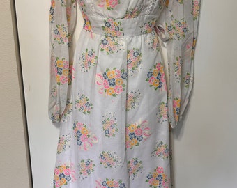 Puede incluir: Un vestido blanco de manga larga con estampado floral de ramos rosas, amarillos y azules. El vestido tiene un escote cuadrado y un corpiño ajustado. Las mangas están fruncidas en las muñecas.