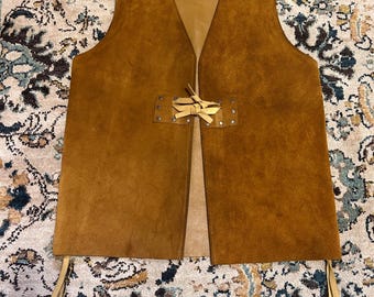 May include: A brown suede vest with a V-neck and a leather tie closure. The vest has a tan interior and leather ties at the bottom. The vest is a medium brown color.