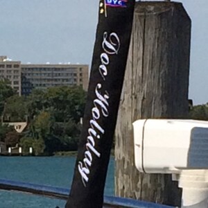 May include: Black boat dock flag with white text that reads "Doc Holiday" and a small blue and white flag with the letters "DVC" on it.
