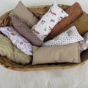 Könnte beinhalten: Eine Sammlung rechteckiger Stoffbeutel in einem geflochtenen Korb. Die Beutel weisen verschiedene Texturen und Muster auf, darunter einen weißen Fuchsdruck, braune Punkte, ein Nähmotiv, einen beigen Stoff und ein flauschiges cremefarbenes Textil.