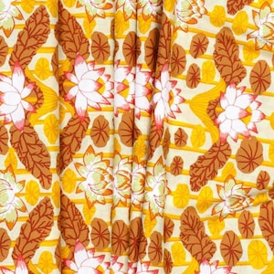 Könnte beinhalten: Ein Stoff mit einem sich wiederholenden Muster aus weißen Lotusblüten mit rosa Akzenten, braunen Blättern und gelben und cremefarbenen Streifen. Das Design ist symmetrisch und detailliert und erzeugt einen visuell reichen Textil.