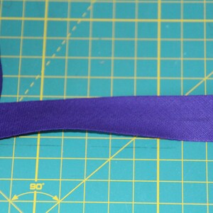 Könnte beinhalten: Eine Rolle violettes Baumwoll-Twillband, etwa 2,5 cm breit, auf einer grünen Schneidematte.