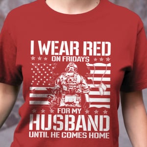 K&ouml;nnte beinhalten: Rotes T-Shirt mit wei&szlig;em Text, der "Ich trage an Freitagen Rot f&uuml;r meinen Mann, bis er nach Hause kommt" lautet. Das Shirt zeigt au&szlig;erdem eine wei&szlig;e Silhouette eines Soldaten, der vor einer amerikanischen Flagge steht.