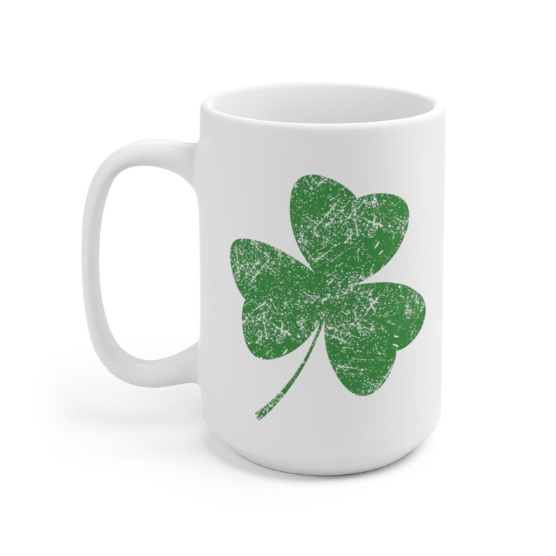 May include: White ceramic mug featuring a distressed green shamrock design. The shamrock is a three-leaf clover, a symbol of luck and Irish heritage. The mug has a large handle for easy gripping and is perfect for hot beverages.