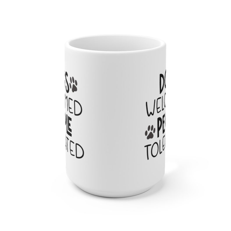 May include: White ceramic coffee mug with black text that reads "Dogs welcomed, people tolerated" on one side and "Dogs welcome, people tolerated" on the other side.