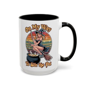 May include: White ceramic mug with a black rim and handle. The mug features a colorful illustration of a witch flying on a broomstick with the text "On My Way To Stir the Pot".