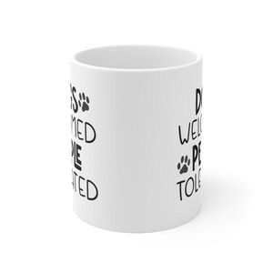 May include: White ceramic mug with black text that reads "Dogs are welcomed, people are tolerated" on one side and "Dogs welcome, people tolerated" on the other side.