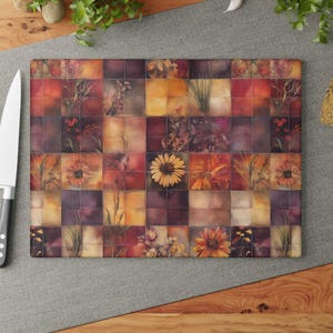 Puede incluir: Tabla de cortar rectangular de vidrio con diseño de mosaico. El diseño presenta elementos florales y botánicos en tonos naranja, amarillo y morado. Un cuchillo de acero inoxidable está a la izquierda. La tabla tiene un patrón de cuadrícula.