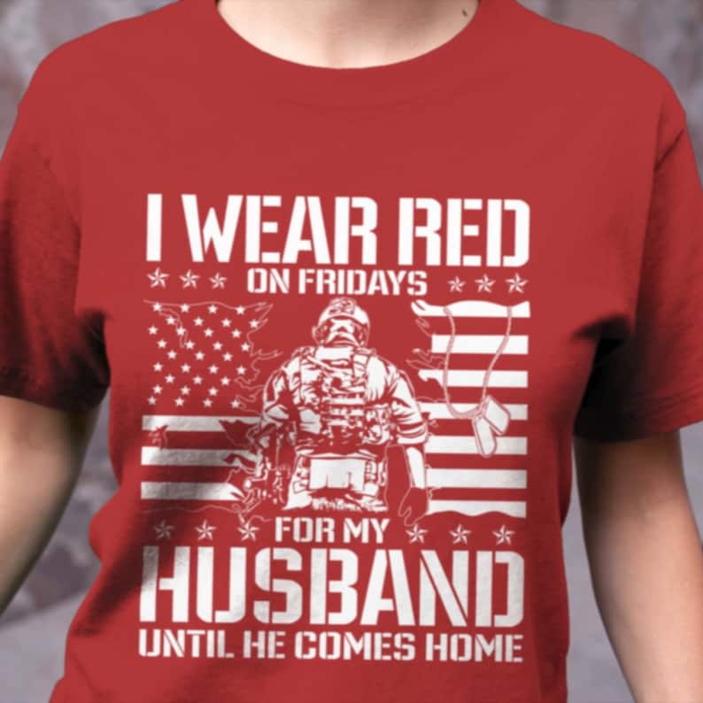 K&ouml;nnte beinhalten: Rotes T-Shirt mit wei&szlig;em Text, der "Ich trage an Freitagen Rot f&uuml;r meinen Mann, bis er nach Hause kommt" lautet. Das Shirt zeigt au&szlig;erdem eine wei&szlig;e Silhouette eines Soldaten, der vor einer amerikanischen Flagge steht.