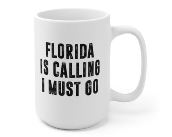 Puede incluir: Taza de cerámica blanca con texto negro que dice "Florida is calling I must go".
