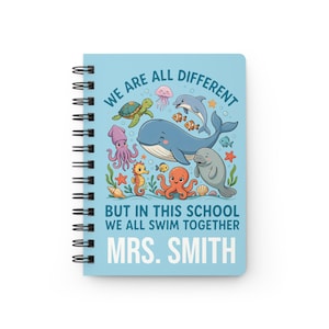 May include: A light blue spiral-bound notebook featuring a colourful illustration of various sea creatures including a whale, dolphin, turtle, octopus, and seahorse. The text reads: WE ARE ALL DIFFERENT BUT IN THIS SCHOOL WE ALL SWIM TOGETHER MRS. SMITH.