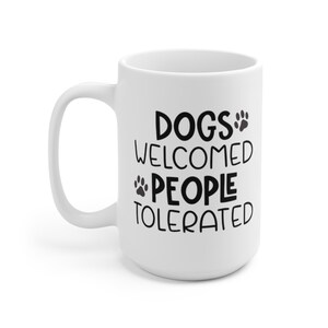 May include: White ceramic coffee mug with black text that reads "Dogs Welcomed People Tolerated" with paw prints.