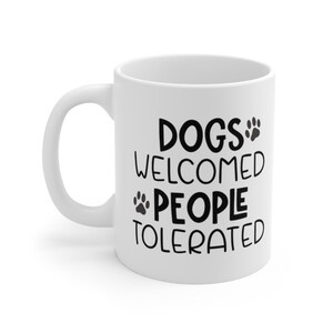 May include: White ceramic coffee mug with black text that reads "Dogs Welcomed People Tolerated" with a paw print graphic.