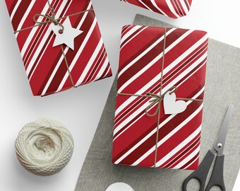 May include: Overhead shot of wrapped gifts with red and white striped paper, tied with twine and white tags. A ball of twine, scissors, and additional tags are also visible, suggesting a crafting or gift-giving theme.