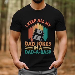 May include: A black t-shirt with a retro-style graphic of a floppy disk and the text "I keep all my dad jokes in a dad-a-base".