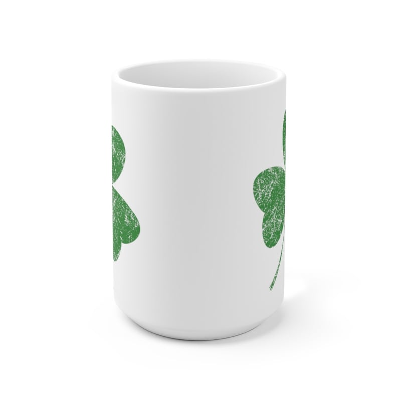May include: White ceramic mug featuring two distressed green shamrock designs. The shamrocks are a classic symbol of St. Patrick's Day. The mug is a standard size for coffee or tea.