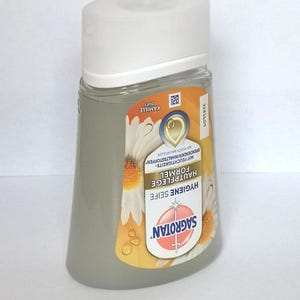Puede incluir: Una botella transparente en forma de pera de jab&oacute;n de higiene Sagrotan con tapa blanca. La etiqueta presenta el nombre de la marca, detalles del producto y un dise&ntilde;o de flor de manzanilla. La botella contiene un l&iacute;quido gris claro.