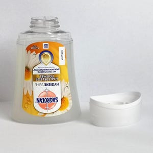 Puede incluir: Una botella de pl&aacute;stico transparente de jab&oacute;n de higiene Sagrotan con una etiqueta amarilla y blanca con flores de manzanilla. La botella est&aacute; junto a un jabonera blanca semicircular. La etiqueta incluye el texto "HYGIENE SEIFE".