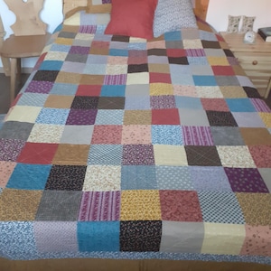 Könnte beinhalten: Eine Patchwork-Decke mit einer Vielzahl von Farben und Mustern, darunter Rot, Blau, Gelb und Braun. Die Decke besteht aus Quadraten aus verschiedenen Stoffen und liegt auf einem Bett mit Kissen.