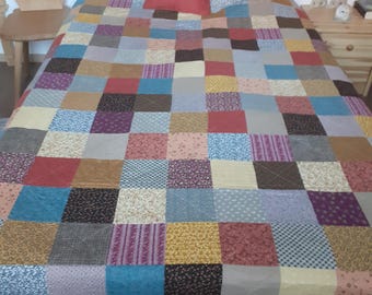 Könnte beinhalten: Eine Patchwork-Decke mit einer Vielzahl von Farben und Mustern, darunter Rot, Blau, Gelb und Braun. Die Decke besteht aus Quadraten aus verschiedenen Stoffen und liegt auf einem Bett mit Kissen.