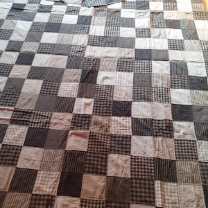 Könnte beinhalten: Eine Patchwork-Decke mit einem karierten Muster in Grautönen und Weiß. Die Decke besteht aus vielen Quadraten aus verschiedenen Stoffen, die ein einzigartiges und strukturiertes Aussehen erzeugen.