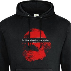 Puede incluir: Sudadera con capucha negra con un gráfico rojo de una cara barbuda y el texto "Nothing to lose but your chains". La sudadera tiene un bolsillo delantero y una capucha con cordón. El gráfico está centrado en el pecho.