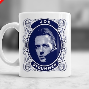 Może przedstawiać: Biały kubek ceramiczny z niebiesko-białym obrazkiem Joe Strummera, wokalisty The Clash. Obrazek jest ozdobiony dekoracyjną ramką.