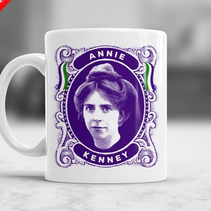 May include: White ceramic mug with a purple and green image of Annie Kenney. The image is framed with a decorative border and includes the text "Annie Kenney".
