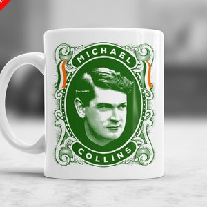 Op de afbeelding: Een witte keramische mok met een groen en oranje ontwerp met een portret van Michael Collins. Het ontwerp is omlijst met een decoratieve rand en de tekst "MICHAEL COLLINS" is onder het portret gedrukt.