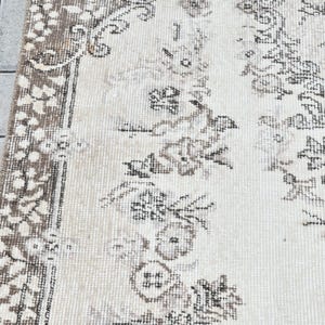 Peut inclure: Un tapis blanc avec un motif floral brun. Le tapis a une bordure &agrave; franges.