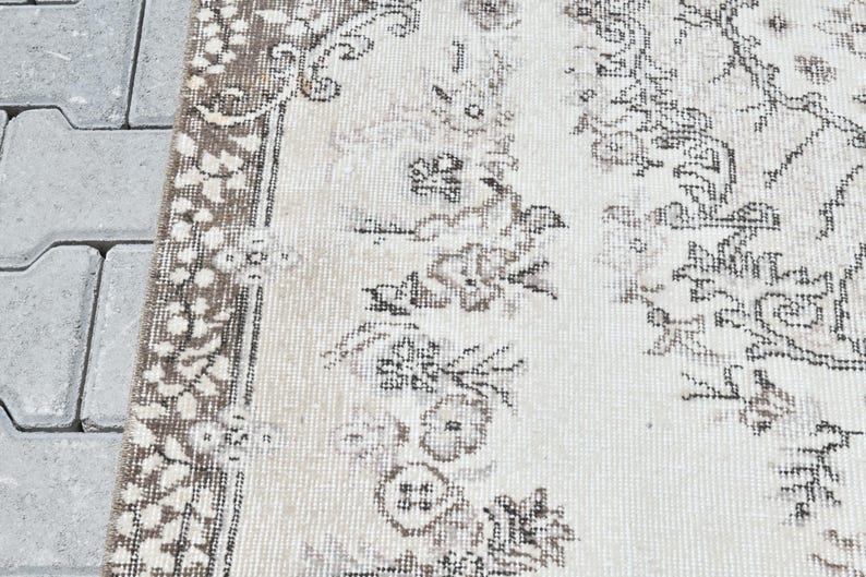 Peut inclure: Un tapis blanc avec un motif floral brun. Le tapis a une bordure &agrave; franges.