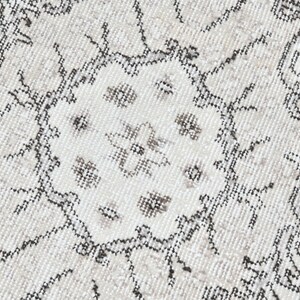 Peut inclure: Gros plan sur un tapis blanc avec un motif g&eacute;om&eacute;trique noir et gris. Le motif pr&eacute;sente un m&eacute;daillon central avec des motifs floraux r&eacute;p&eacute;t&eacute;s.