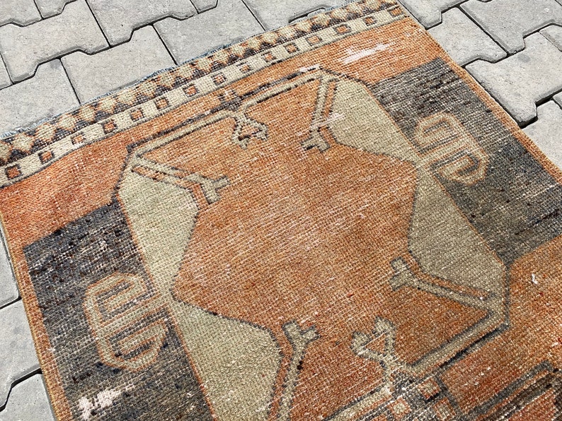 Pu&ograve; includere: Un tappeto vintage con un motivo geometrico in tonalit&agrave; di marrone, beige e nero. Il tappeto ha un aspetto usurato e sbiadito, che gli conferisce un aspetto rustico e antico.