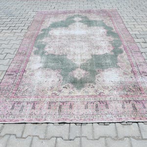 Può includere: Un tappeto vintage con un centro verde sbiadito e un bordo rosa. Il tappeto ha un aspetto usurato ed è fatto di lana.