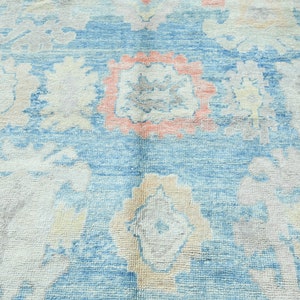 K&ouml;nnte beinhalten: Ein Vintage-Teppich mit blauem Hintergrund und einem floralen Muster in Rosa-, Wei&szlig;- und Graut&ouml;nen.