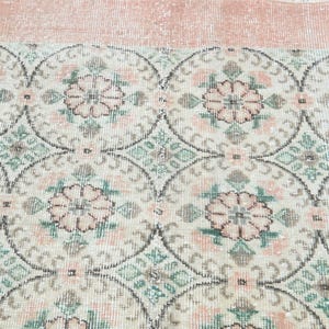 May include: A vintage rug with a repeating pattern of pink flowers and green leaves on a white background. The rug has a light pink border.
