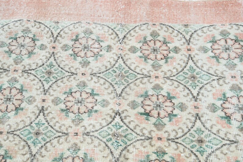 May include: A vintage rug with a repeating pattern of pink flowers and green leaves on a white background. The rug has a light pink border.