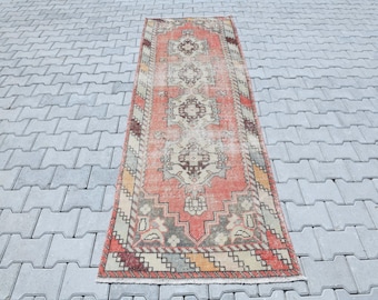 May include: A vintage runner rug with a traditional Persian design in shades of red, orange, and cream. The rug has a distressed look with faded colors and a worn texture.