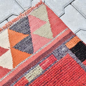 May include: A colorful woven rug with geometric patterns in shades of red, orange, black, and white. The rug has a fringed edge and is made of a thick, textured material.