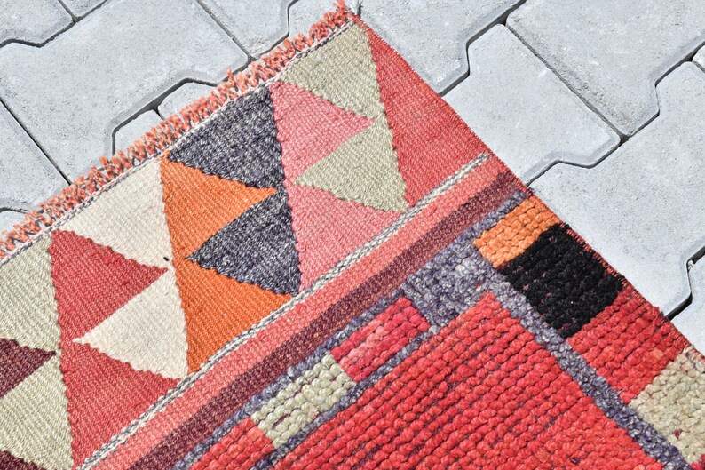 May include: A colorful woven rug with geometric patterns in shades of red, orange, black, and white. The rug has a fringed edge and is made of a thick, textured material.