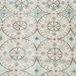 May include: A vintage rug with a repeating pattern of floral motifs in shades of pink, green, and white.