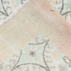 May include: Close-up of a light pink and cream colored rug with a floral pattern. The rug has a fringe border and is made of a soft, woven material.