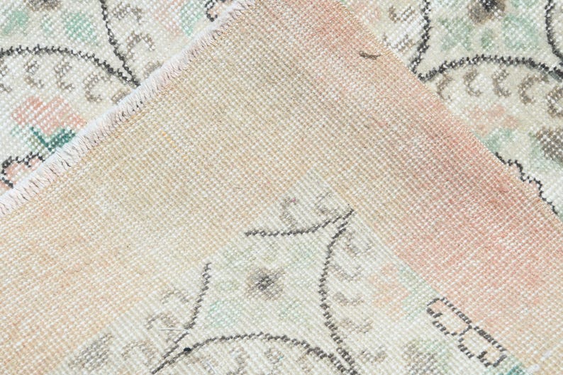 May include: Close-up of a light pink and cream colored rug with a floral pattern. The rug has a fringe border and is made of a soft, woven material.