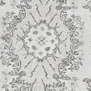 Peut inclure: Un tapis blanc avec un motif floral noir et gris. Le tapis a un aspect vieilli, avec certaines parties du noir et du gris d&eacute;lav&eacute;es.